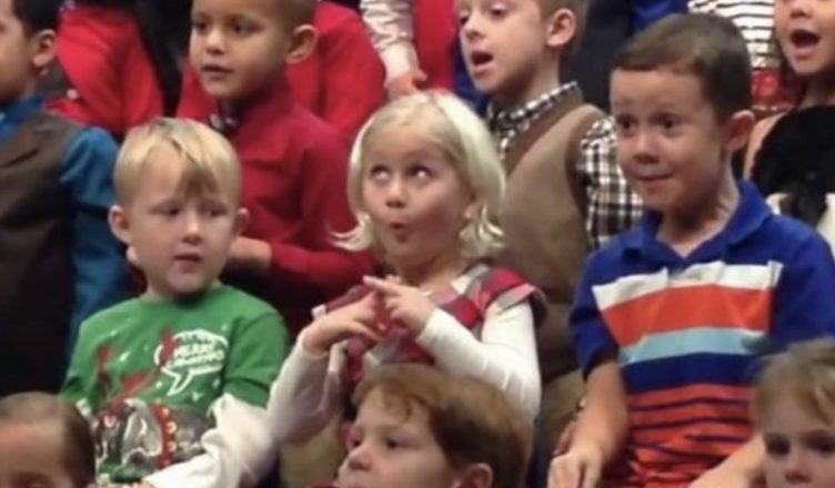 During a kindergarten holiday concert, a little girl delightfully signs to her deaf parents, creating an unforgettable moment